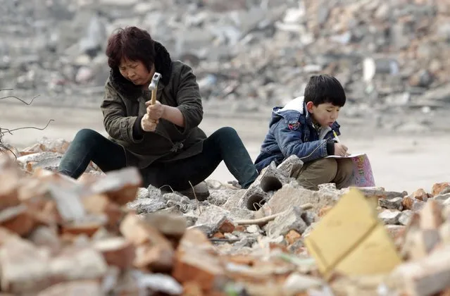 Primary school student Lele (R), 7, does his homework as his grandmother smashes concrete to look for recyclable steel bars at a demolition site in Zhengzhou, Henan province February 3, 2015. Lele's father was diagnosed with Leukemia four years ago and the family has been struggling to pay the medical bills. (Photo by Reuters/Stringer)