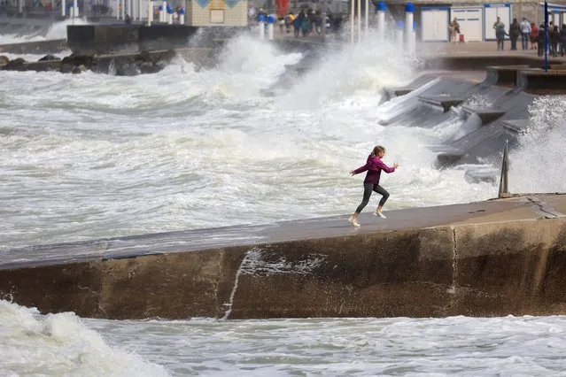 A girl runs on a dike as waves crash against a breakwater at high tide in Wimereux as gusty summer winds hit northern and western France on August 2, 2023. (Photo by Pascal Rossignol/Reuters)
