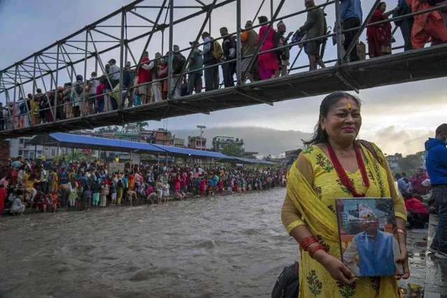 A devotee poses for a photograph holding a portrait of her late father after performing rituals on the banks of the Bagmati river during “Kuse Aunsi” at the Gokarneshwor Temple, Kathmandu, Nepal, Thursday, September 14, 2023. Kuse Aunsi is a festival of Nepal where fathers, living or dead, are honored. Children with living fathers show their appreciation by giving presents and sweets and those whose fathers are deceased pay tributes at the Gokarneshwar temple. (Photo by Niranjan Shrestha/AP Photo)