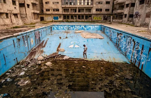 A man with his camera walks inside an abandoned swimming pool in Havana, on August 3, 2023. With the current hot summer, Havana residents have rushed to the dilapidated natural pools on the coast of their city, built by wealthy families in the first half of the last century. (Photo by Yamil Lage/AFP Photo)