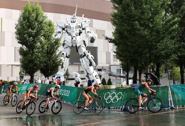 Athletes compete in women's triathlon in front of a life-size Unicorn Gundam statue in rainfall and wind caused by tropical storm Nepartak at the Odaiba Marine Park in Tokyo on July 27, 2021, during the Tokyo 2020 Olympic Games. (Photo by Issei Kato/Reuters)