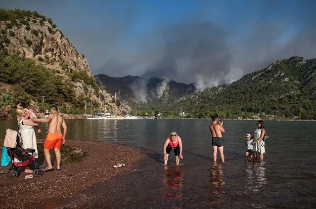 People spend time at the sea backdropped by the wildfires burning in Marmaris district of Mugla, Turkey, 31 July 2021. According to a statement by the Turkish government's Disaster and Emergency Management Presidency (AFAD) released on 30 July 2021, at least three people lost their lives and some 271 others were affected by blazes that swept through the country's southern coast. (Photo by Erdem Sahin/EPA/EFE)