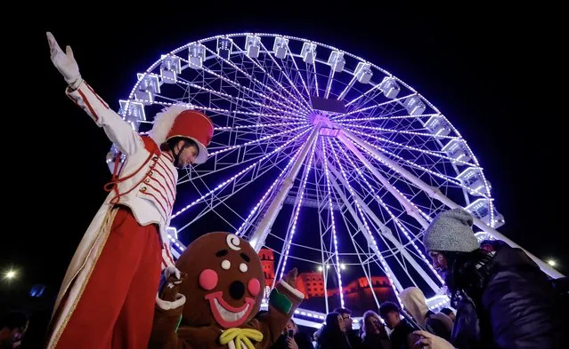 A children's entertainer gestures, backed by a Ferris wheel illuminated with Christmas lights, shortly after the official opening of the Christmas market in downtown Bucharest, Romania, 30 November 2023. Romania, an Orthodox-Christian country, celebrates Christmas on 25 December. (Photo by Robert Ghement/EPA)