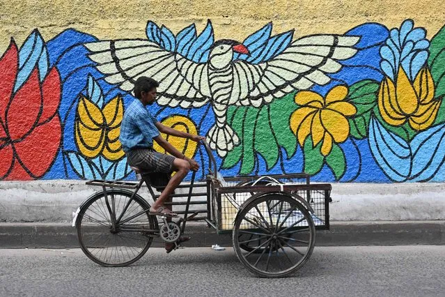 A man rides a bicycle cart along a road past a mural in Chennai on September 12, 2023. (Photo by R. Satish Babu/AFP Photo)