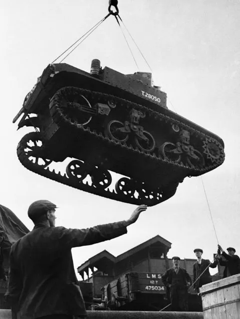 The dockyard Tic-Tic Man in the foreground gives the signal and other dockers guide an American tank to rest on a British quayside, pictorial evidence of the real help that America is giving the British war effort, July 8, 1941. The tank is being loaded on to an English railway wagon at a British port ready to be delivered to army headquarters. (Photo by AP Photo)
