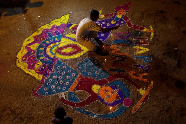 A boy lights candles on a rangoli, or mural made out of coloured powders outside his home during Diwali, the Hindu festival of lights, in Karachi, Pakistan on November 4, 2021. (Photo by Akhtar Soomro/Reuters)