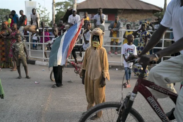 A kid wears a costume as supporters of the Gambian President Adama Barrow celebrate the partial results that give the lead to their candidate during the counting ballots in Gambia's presidential election, in Banjul, Gambia, Sunday, December 5, 2021. (Photo by Leo Correa/AP Photo)