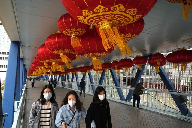 People wearing face masks, walk past decorations on a bridge to celebrate the Lunar New Year in Hong Kong, Tuesday, January 18, 2022. Hong Kong police arrested two former flight attendants for allegedly leaving their homes when they should have been in isolation for possible coronavirus infections, which were later confirmed. (Photo by Kin Cheung/AP Photo)