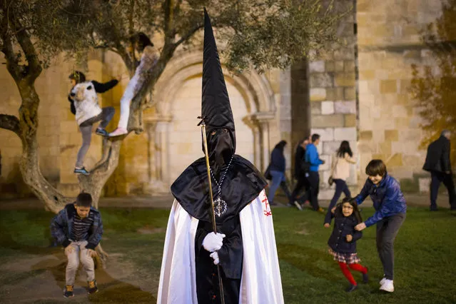 Children play in the background as a penitent watches a march from “Jesus en su Tercera Caída” brotherhood during a procession in Zamora, Spain, Monday, April 14, 2014. Hundreds of processions take place throughout Spain during the Easter Holy Week. (Photo by Andres Kudacki/AP Photo)