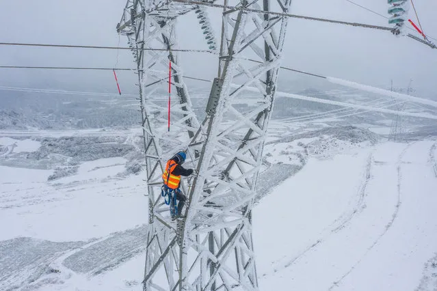 This photo taken on February 21, 2022 shows a worker climbing a pylon to remove ice from electric transmission lines as it snows in Bijie in China's southwestern Guizhou province. (Photo by AFP Photo/China Stringer Network)