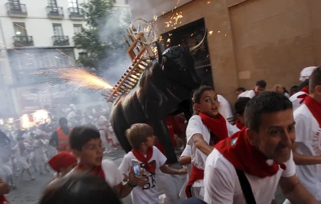 Revellers run from the “Fire Bull”, a man carrying a metal structure shaped like a bull and loaded with fireworks, on the second day of the San Fermin festival in Pamplona, northern Spain, July 7, 2015. Visitors to the nine-day festival, depicted in Ernest Hemingway's 1926 novel “The Sun Also Rises”, take part in activities including The Running Of The Bulls, an early morning half mile dash from the corral to the bullring alongside six bulls destined to die in the afternoon's corrida. (Photo by Joseba Etxaburu/Reuters)