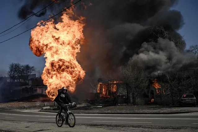 A cyclist rides past flames and smoke rising from a fire following an artillery fire on the 30th day of the invasion of Ukraine by Russian forces in the northeastern city of Kharkiv on March 25, 2022. Russian strikes targeting a medical facility in Kharkiv on March 25, 2022, killed at least four civilians and wounded several others, Ukrainian officials said. (Photo by Aris Messinis/AFP Photo)