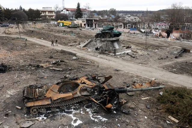 Local residents pass by a damaged Russian tank in the town of Trostyanets, east of capital Kyiv, Ukraine, Monday, March 28, 2022. The monument to Second World War is seen in background. (Photo by Efrem Lukatsky/AP Photo)