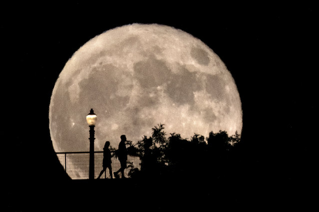 People walk in front of a rising supermoon at Griffith Observatory in Los Angeles, Monday, August 19, 2024. (Photo by Richard Vogel/AP Photo)