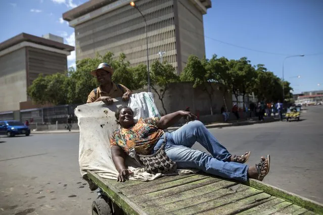 In the November 19, 2019 photo, Neyda Rosa Hernandez poses for a photo with her husband Osmar Fernandez while reclining on the cart she uses to sell bananas, in Maracaibo, Venezuela. Pictured in the background are offices of the state oil company PDVSA. Critics blame two decades of socialist rule for destroying the oil industry, that today produces a fraction of what it did at its height two decades ago. The Venezuelan government blames U.S. sanctions for many of its problems. (Photo by Rodrigo Abd/AP Photo)