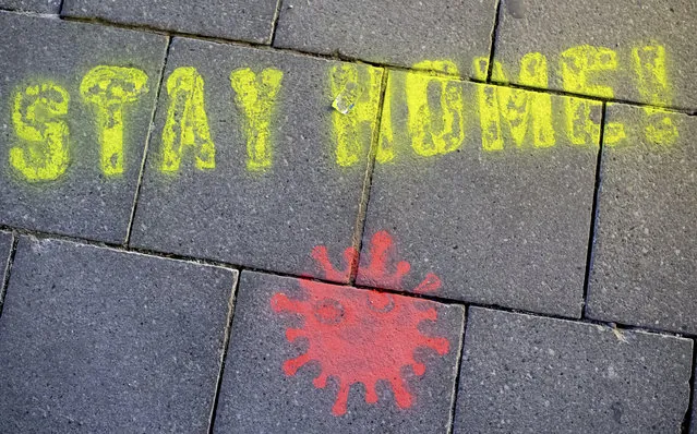 A graffiti consisting of the text “Stay Home” and a symbolic novel coronavirus has been sprayed on the ground in Munich, Germany, Monday March, 16, 2020. Berlin has closed all Bars and pubs because of the corona virus outbreak in Germany. For some, especially older adults and people with existing health problems, it can cause more severe illness, including pneumonia. (Photo by Sven Hoppe/dpa via AP Photo)