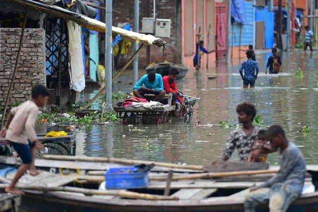 Youths living in a low lying area on the banks of the River Ganges sit on cart in a flooded street at Daraganj area in Allahabad on August 19, 2022, after water levels rose following monsoon rains. (Photo by Sanjay Kanojia/AFP Photo)