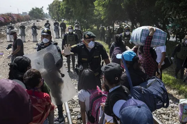 A policeman talks to day laborers and informal workers at a police blockade on the outskirts of Lima, Peru, Saturday, April 18, 2020. Because the strict quarantine rules amid the new coronavirus pandemic do not allow for inter-province travel, the workers have been living on the side of the road for days blocked by police from returning to their homes which are located outside the capital. (Photo by Rodrigo Abd/AP Photo)