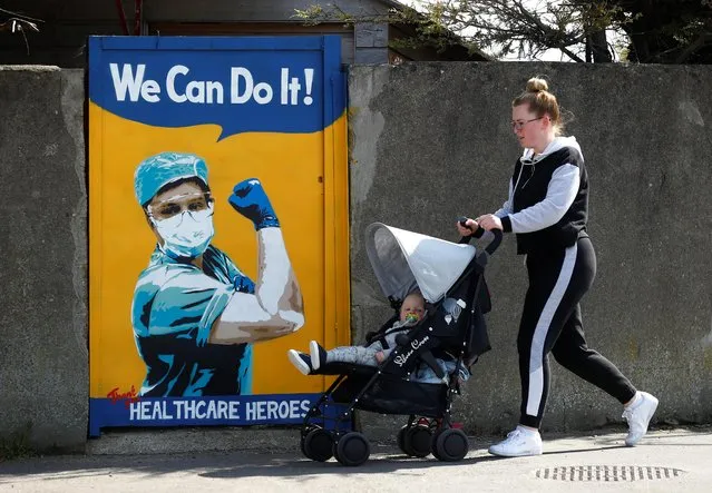 A woman pushes a child in a buggy past a mural by Emma Blake, as the spread of the coronavirus disease (COVID-19) continues, Dublin, Republic of Ireland, April 21, 2020. (Photo by Jason Cairnduff/Reuters)