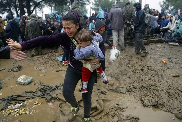 A Syrian refugee carries her baby as she walks through the mud to cross the border from Greece into Macedonia during a rainstorm, near the Greek village of Idomeni, September 10, 2015. (Photo by Yannis Behrakis/Reuters)