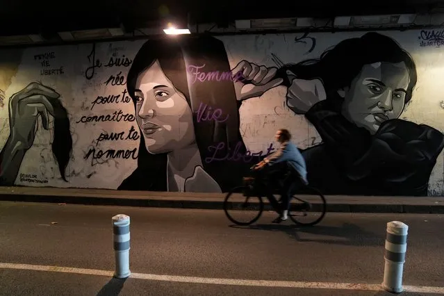 A woman rides bicycle front of a mural signed by Clacks-one and Heartcraft_Street art, depicting women cutting their hair to show support for Iranian protesters standing up to their leadership over the death of a young woman in police custody, in a tunnel in Paris, France, Wednesday, October 5, 2022. Thousands of Iranians have taken to the streets over the last two weeks to protest the death of Mahsa Amini, a 22-year-old woman who had been detained by Iran's morality police in the capital of Tehran for allegedly not adhering to Iran's strict Islamic dress code. Mural reads : “I was born to know you to name you”, “Woman Life Freedom”. (Photo by Francois Mori/AP Photo)
