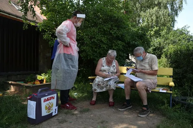 Local residents fill in documents as a member of an electoral commission stands nearby with a mobile ballot box during a seven-day vote on constitutional reforms, in the village of Troitskoye in Moscow region, Russia on June 25, 2020. (Photo by Evgenia Novozhenina/Reuters)