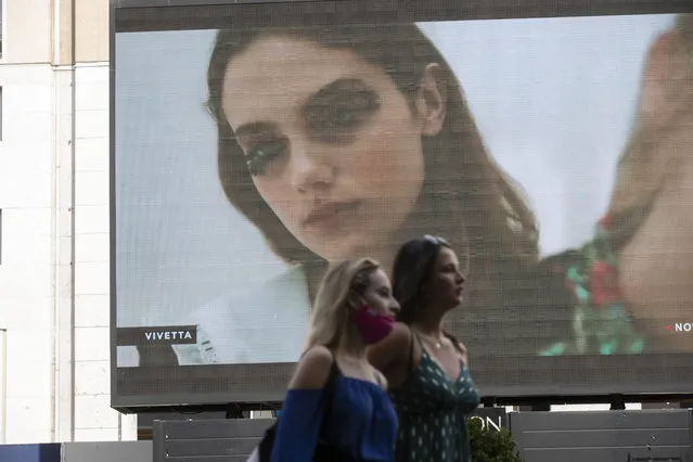 Pedestrians pass by a screen showing a Vivetta model during the Milan Digital Fashion Week, in Milan, Italy, Tuesday, July 14, 2020. Forty fashion houses are presenting previews of menswear looks for next spring and summer and pre-collections for women in digital formats, due to concerns generated by the COVID-19. (Photo by Luca Bruno/AP Photo)