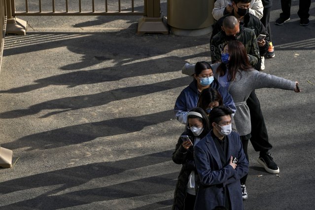 A woman wearing a face mask stretches her arms as she and masked residents wait in line for their routine COVID-19 tests at a coronavirus testing site in Beijing, Wednesday, November 16, 2022. (Photo by Andy Wong/AP Photo)