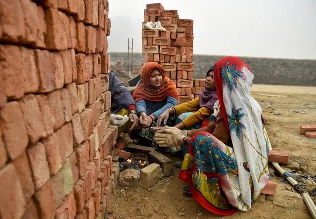 Indian women laborers working at a building construction site sit around a fire to warm their hands on a cold and foggy morning in Greater Noida, India, Friday, January 5, 2018. Most parts of northern India has been experiencing cold weather conditions. (Photo by R.S. Iyer/AP Photo)