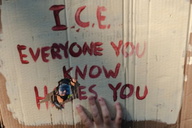 A police officer's face can be seen through a hole in a protester's sign outside of the Robert Young Federal Building on June 9, 2025 in Downtown Los Angeles, California. Tensions in the city remain high after the Trump administration called in the National Guard against the wishes of city leaders. (Photo by Jim Vondruska/Getty Images/AFP Photo)