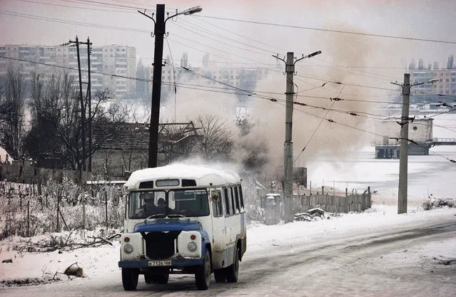 A bus drives past as smoke rises from a building which had been repeatedly hit by tank shells in the southwest of Grozny, January 24, 1995. Fighting intensified accompanied by rocket and tank fire. (Photo by Karsten Thielker/AP Photo/File)