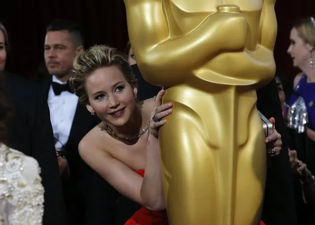 Jennifer Lawrence, best supporting actress nominee for her role in the film “American Hustle”, peeks around an Oscar statue on the red carpet as actor Brad Pitt (L) looks on at the 86th Academy Awards in Hollywood, California, in this March 2, 2014 file photo. (Photo by Adrees Latif/Reuters)