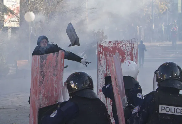 A supporter of the opposition parties in Kosovo throws a rock towards police in riot gear securing Kosovo's parliament building, in capital Pristina on Tuesday, November 17, 2015. Kosovo opposition used tear gas and pepper spray inside parliament and pelted police with rocks and pink paint outside the building in another attempt to force the government to renounce recent deals with Serbia and Montenegro. (Photo by Visar Kryeziu/AP Photo)