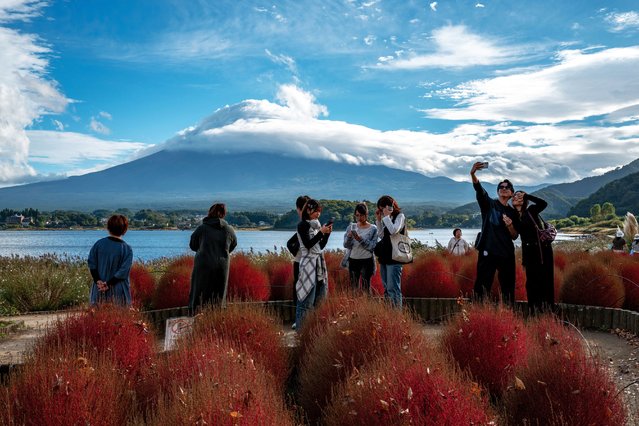 Tourists take pictures as cloud-clad Mount Fuji is seen in the background from Oishi park in the town of Fujikawaguchiko, Yamanashi prefecture on October 18, 2025. (Photo by Philip Fong/AFP Photo)