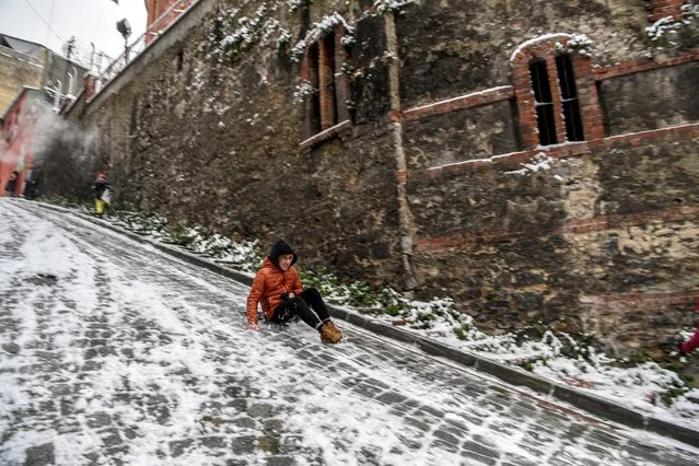 A young man slides on a snow covered street in the Balat District of Istanbul on January 18, 2021. (Photo by Ozan Kose/AFP Photo)