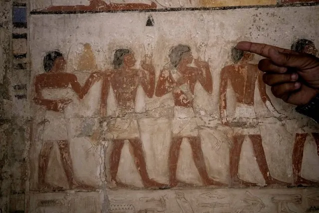 An Egyptian archeologist points at a colored painting showing offering sacrifices at a recently uncovered tomb that was said to belong to a top official of the fifth Dynasty named "Ne Hesut Ba" (2400 BC), at the site of the Step Pyramid of Djoser in Saqqara, 24 kilometers (15 miles) southwest of Cairo, Egypt, Saturday, May 27, 2023. (Photo by Amr Nabil/AP Photo)