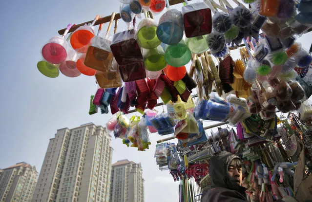 A Chinese stall vendor is seen with as household goods are hung on poles above his stall at a market in Beijing, China, 14 January 2016. China will announce its fourth-quarter and full-year 2015 economic growth data on 19 January amid continued concern over the slowing of the world's second-largest economy. (Photo by How Hwee Young/EPA)