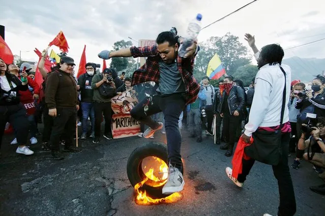 A university student leaps over a burning tyre during a demonstration against the government of President Guillermo Lasso in the framework of indigenous-led protests that began on the eve, in downtown Quito on June 14, 2022. Ecuadoran police on June 14 announced the arrest of a top indigenous leader, Leonidas Iza, who has spearheaded a nationwide protest movement against high fuel prices. (Photo by Veronica Lombeida/AFP Photo)