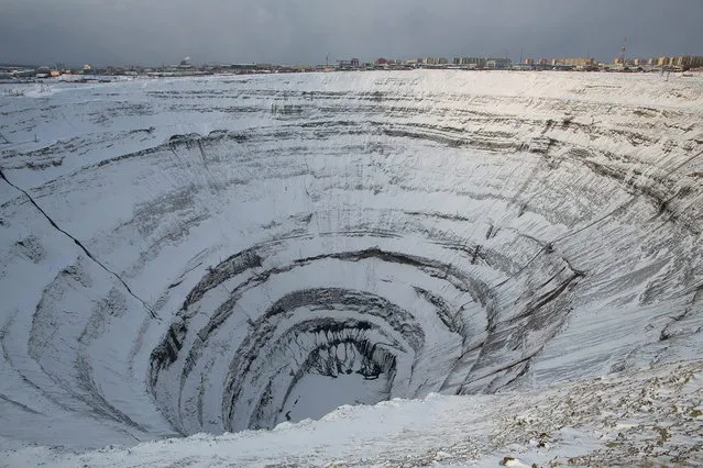 City buildings stand beyond the giant excavated hole left by the Mir mine, a former open pit diamond mine, in Mirny, Russia, on Tuesday, November 12, 2013. OAO Alrosa, the world's largest diamond producer, raised about $1.3 billion in an oversubscribed share sale from investors including Oppenheimer Funds Inc. and Lazard Ltd.'s asset-management unit, First Deputy Prime Minister Igor Shuvalov said. (Photo by Andrey Rudakov/Bloomberg)