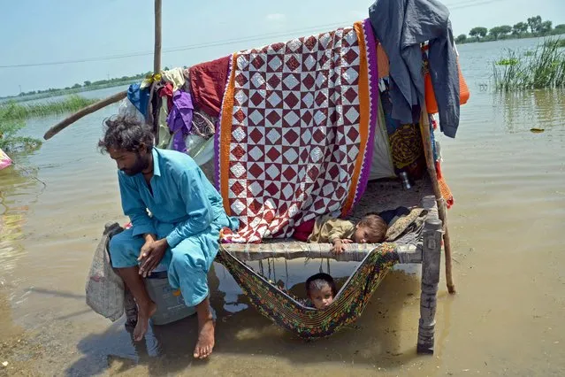 A flood-affected man sits along with his children alongside flood waters after heavy monsoon rains in Jaffarabad district of Balochistan province on August 31, 2022. Army helicopters flew sorties over cut-off areas in Pakistan's mountainous north on August 31 and rescue parties fanned out across waterlogged plains in the south as misery mounted for millions trapped by the worst floods in the country's history. (Photo by Fida Hussain/AFP Photo)