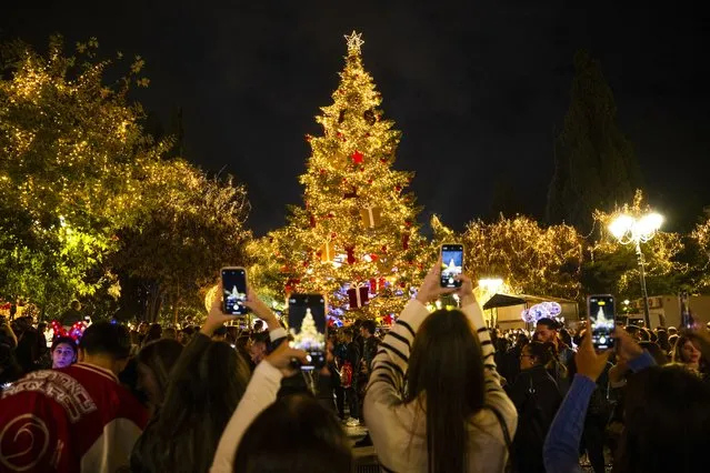 Pedestrians use their smartphones to capture the newly illuminated Christmas tree at the Syntagma square in Athens on November 23, 2023. (Photo by Angelos Tzortzinis/AFP Photo)