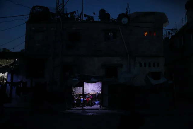 A Palestinian man sits as he sells vegetables in a makeshift shop lit with a lamp powered by a battery during a power cut in Beit Lahiya in the northern Gaza Strip January 11, 2017. (Photo by Mohammed Salem/Reuters)