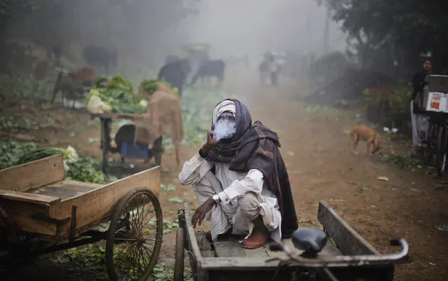 An Indian laborer, wrapped in a blanket, smokes while sitting in his rickshaw on a foggy morning in New Delhi, India, Tuesday, December 17, 2013. Delhi and other parts of northwest India witnessed the first dense fog of the season that threw air and rail traffic out of gear, more than a week before it was expected, according to local news reports. (Photo by Altaf Qadri/AP Photo)