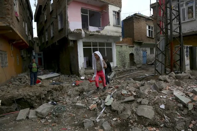 Children walk past by damaged buildings in Sur district, which is partially under curfew, in the Kurdish-dominated southeastern city of Diyarbakir, Turkey February 19, 2016. Three Turkish soldiers were killed and four others were lightly injured after a building collapsed in the southeast, where security forces have been clashing with Kurdish militants for months. (Photo by Sertac Kayar/Reuters)