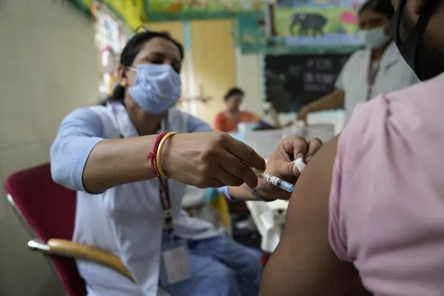 A health worker administers the vaccine for COVID-19 at a vaccination center set up at a government-run school in New Delhi, India, Tuesday, September 21, 2021. India, the world's largest vaccine producer, will resume exports and donations of surplus coronavirus vaccines in October after halting them during a devastating surge in domestic infections in April, the health minister said Monday. (Photo by Manish Swarup/AP Photo)