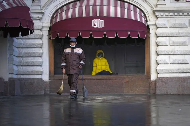 A municipal worker walks past a window of GUM, the State Shop in Red Square, closed due to the coronavirus in Moscow, Russia, Thursday, October 28, 2021. Moscow followed Thursday, shutting kindergartens, schools, gyms, entertainment venues and most stores, and allowing restaurants and cafes to only provide service for takeout or delivery. The number of new daily cases in Russia rose by over forty thousand on Thursday, topping a previous record reached earlier this week. The government hopes that the nonworking period will help curb the spread by keeping most people out of offices and public transportation. (Photo by Alexander Zemlianichenko/AP Photo)