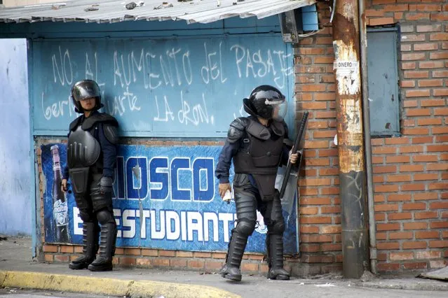 Police officers take cover at a corner of a street while clashing with demonstrators during a protest against the increase in the price of public transport in San Cristobal March 29, 2016. (Photo by Carlos Eduardo Ramirez/Reuters)