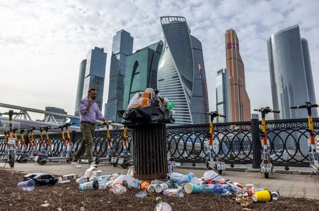 A man walks past an overflowing trash can next to skyscrapers of Moscow International Business District, also known as Moskva-City, in Moscow, Russia on April 2, 2024. (Photo by Maxim Shemetov/Reuters)