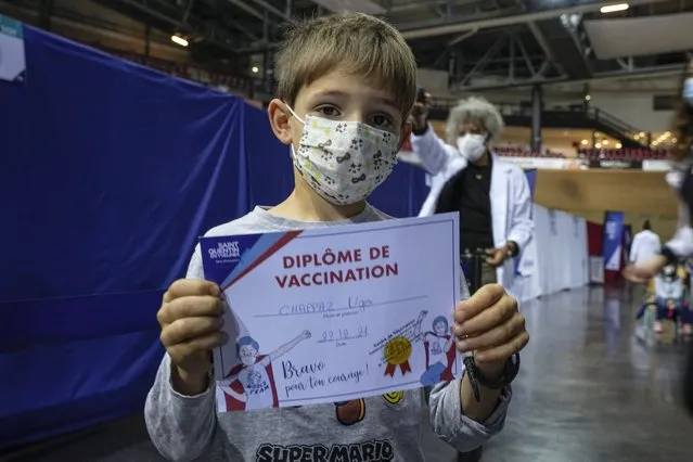 Hugo Chappaz, 9, displays his vaccination diploma at the National Velodrome in Saint-Quentin-en-Yvelines, west of Paris, France, Wednesday, December 22, 2021. Schoolchildren clung nervously to their parents as they entered a vast vaccinodrome west of Paris, then walked proudly away with a “vaccination diploma” as France kicked off mass vaccinations of children age 5 to 11. (Photo by Michel Euler/AP Photo)