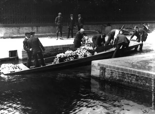 1903: A coffin decked in flowers in a punt, which a group of men are pulling into the mooring